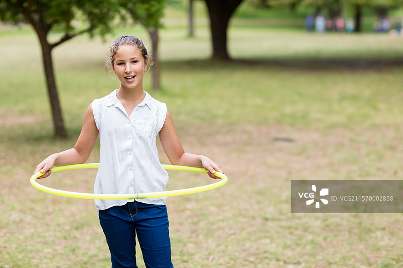 在公园的草坪上，旋转的女孩手里拿着黄色的呼啦圈，围在腰间。图片素材