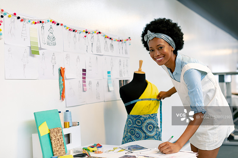 非裔美国女性在工作室中用卷尺和布料样本测量模特上的面料，留有空白空间图片素材