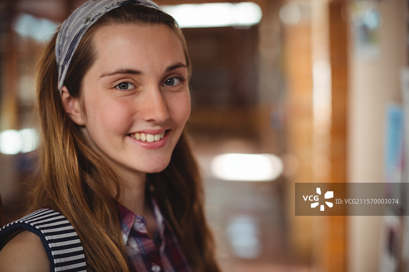 微笑的少女站在学校走廊，手里拿着条纹背包和图案发带图片素材