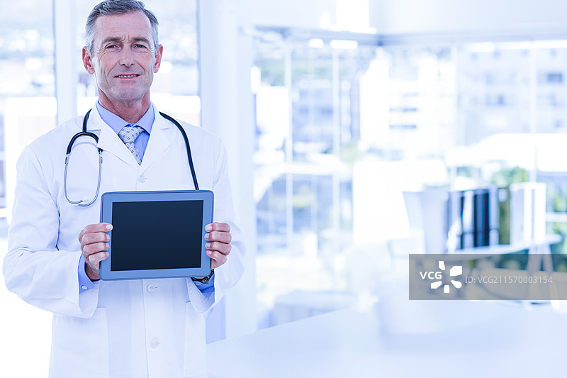 男医生在医疗办公室里手持空白平板，展示听诊器和文件。图片素材