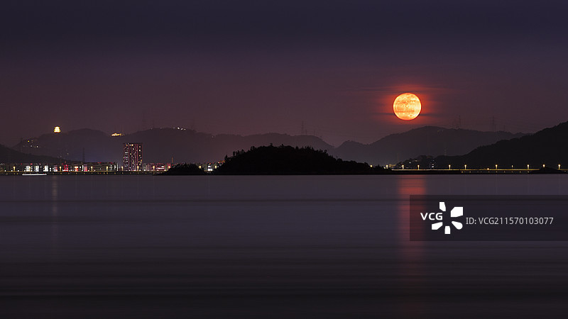 红色满月静谧湖面的倒影城市灯火通明图片素材