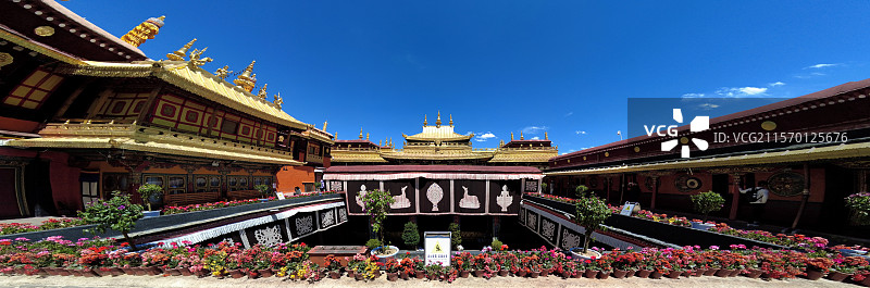 西藏拉萨大昭寺金顶在蓝天映衬下熠熠生辉红墙庄重古朴殿前繁花似锦尽显藏传佛教寺院的庄严与绚丽。图片素材