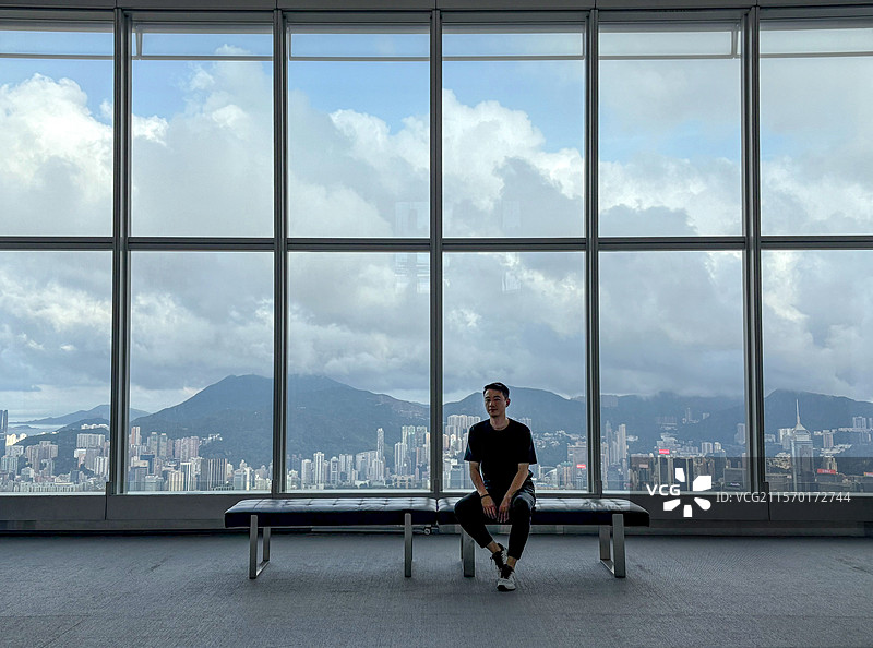 香港环球贸易广场100楼室内观景台 坐在长凳上的男子和他身后的城市天际线图片素材