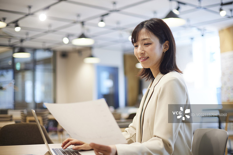 微笑的日本女商人在办公室使用笔记本电脑工作。图片素材