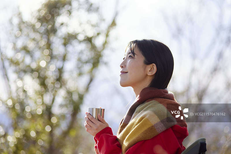 日本女性在冬季山脉中享受户外时光，手中拿着一杯咖啡。图片素材