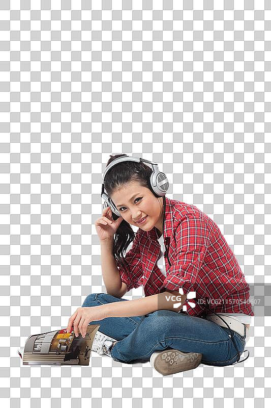 棚拍年轻女人坐在地上听音乐看杂志图片素材