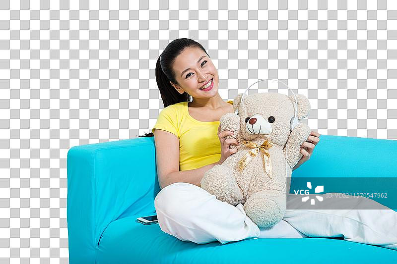 棚拍年轻女人坐在沙发上玩玩具熊图片素材