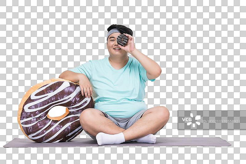 肥胖的青年男子拿着甜甜圈做运动图片素材