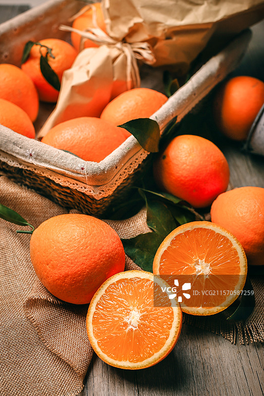 新鲜的橙子散落的放在木纹桌布上和旁边的蓝子里其中还有2块被切成两半图片素材