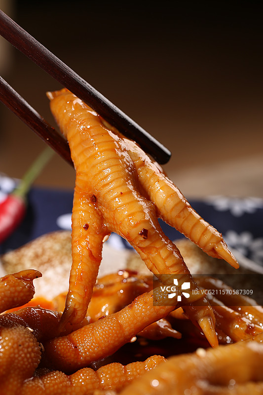 麻辣鸡爪上方用筷子夹着一块油亮的麻辣鸡爪图片素材