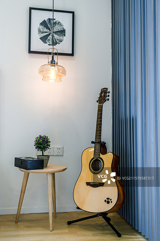 一个简约温馨的角落，墙上挂着黑白照片，透过玻璃灯罩的暖色灯光照亮了空间。旁边是一个小圆桌，上面放着一图片素材