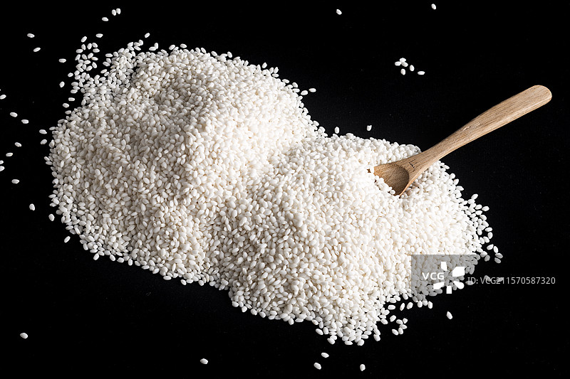 黑色背景中摆放着两堆白白的糯米且有个木勺舀着其中一堆图片素材