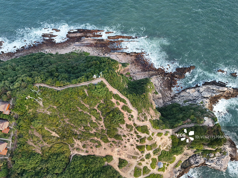 航拍日出时分深圳杨梅坑鹿咀山庄绿意盎然的山体与蓝色海浪拍打礁石的高角度视图图片素材