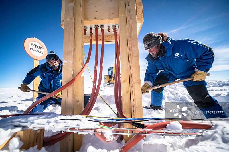 两名技术人员在户外电箱前用铲子完成了在雪中挖沟的工作。夏季，约25名来自不同工种的技术人员在度假村进行各种维护任务。这包括电力分配网络，该网络在寒冷和温度变化的考验下，其需求，特别是科学设施的需求，正在不断增加。康科迪亚的体力劳动尤其艰巨，显然是因为寒冷，也因为缺氧。康科迪亚南极研究站，Dome C高原，东南极。图片素材