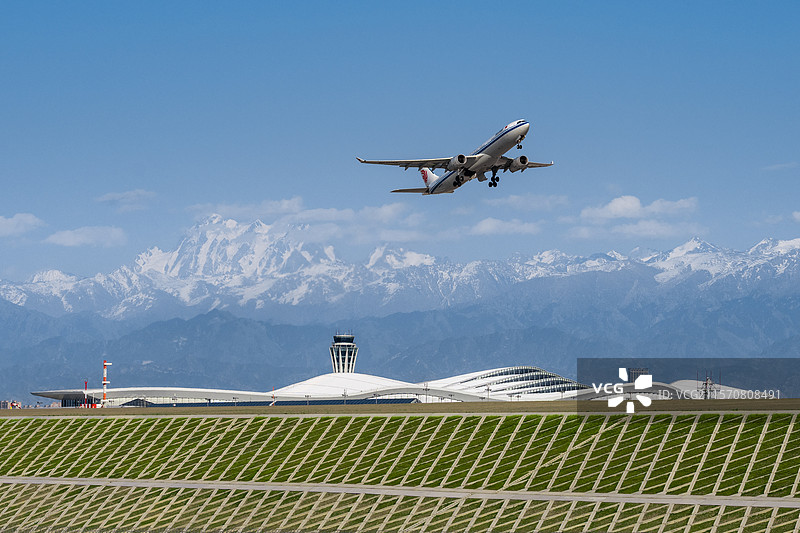 新疆天山山脉博格达峰下，在乌鲁木齐天山国际机场起飞的民航客机图片素材