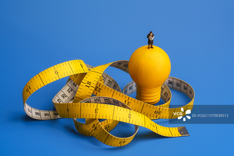 蓝色背景皮尺卷着灯泡上看书的男士微缩创意图片素材