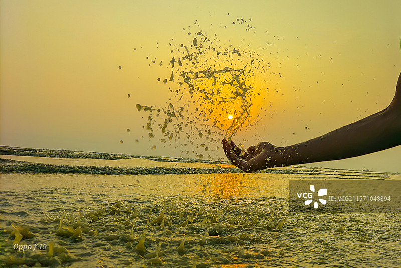 在日落时分，天空下，一个人用手抛撒沙子于海滩。图片素材