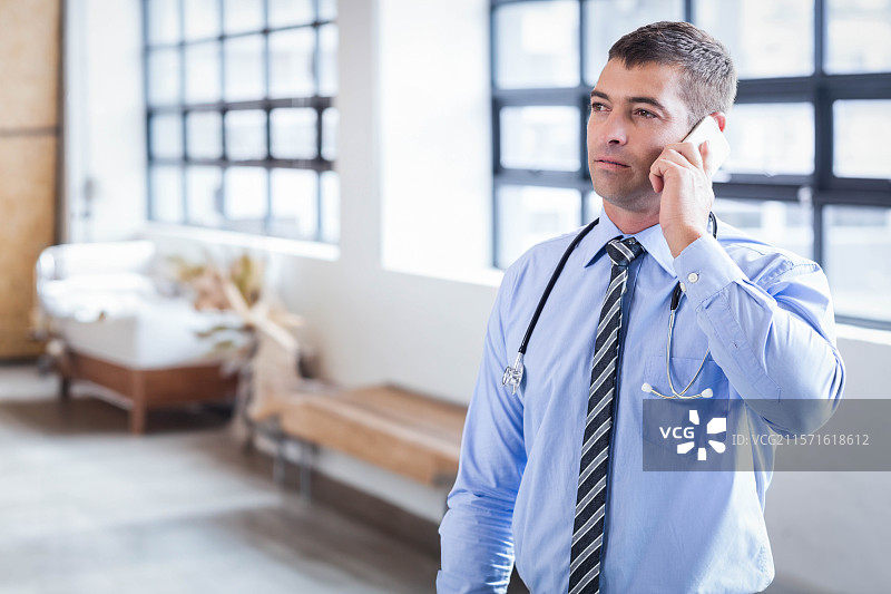 穿着衬衫和领带的男性医生在大堂里用智能手机通话，脖子上挂着听诊器，留有空白空间图片素材