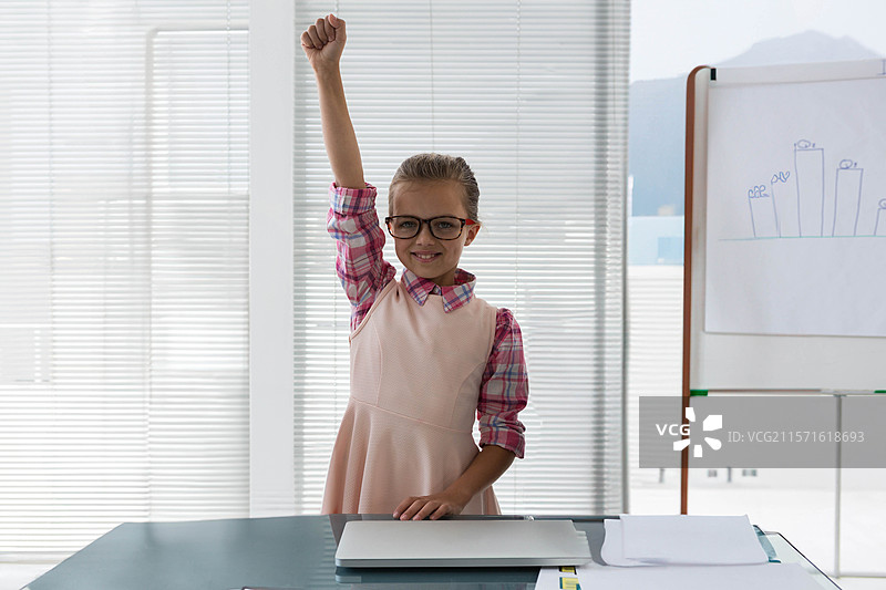 戴眼镜的孩子在教室的桌子上，旁边有笔记本电脑、文件和带有柱状图的翻转图表。图片素材