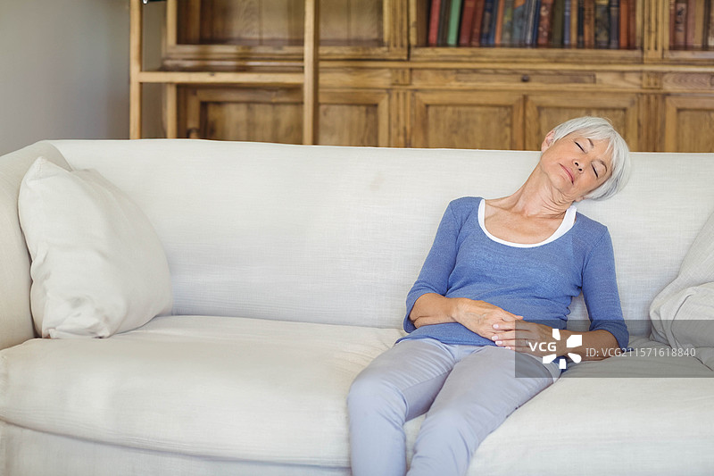 老年女性侧卧在米色沙发上，家中客厅有书架，留有空白空间图片素材