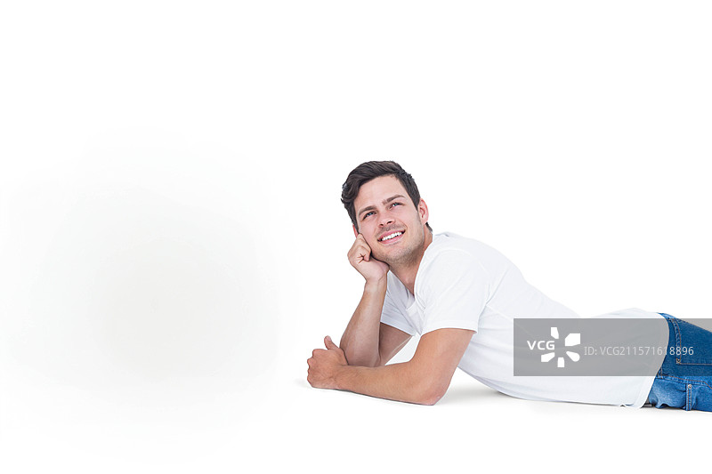 穿着白色T恤和蓝色牛仔裤的男人躺在工作室地板上，支着头微笑着仰望，留有空白空间。图片素材