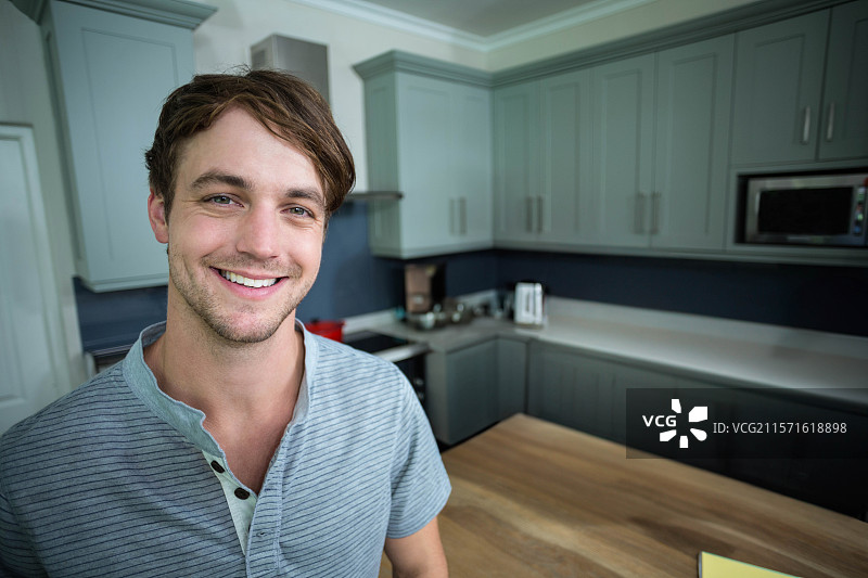 男人微笑着站在家用厨房的岛台旁，旁边有烤面包机、水壶和微波炉。图片素材