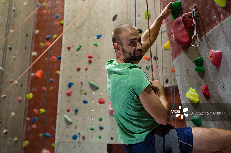 三十多岁的男子在攀岩馆攀爬墙壁，穿着安全带，手握绳索，留有空白空间图片素材