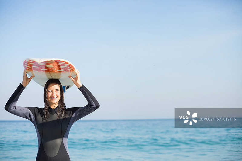 穿着潜水服的女性冲浪者在海岸线的海水中举起冲浪板，留有空白空间。图片素材