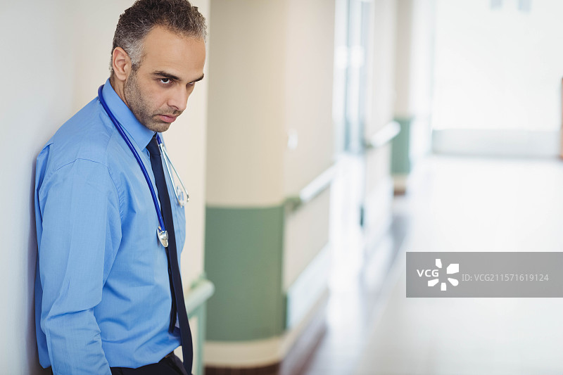 中东男性医生靠在医院走廊的墙上，手持听诊器，留有空白空间图片素材