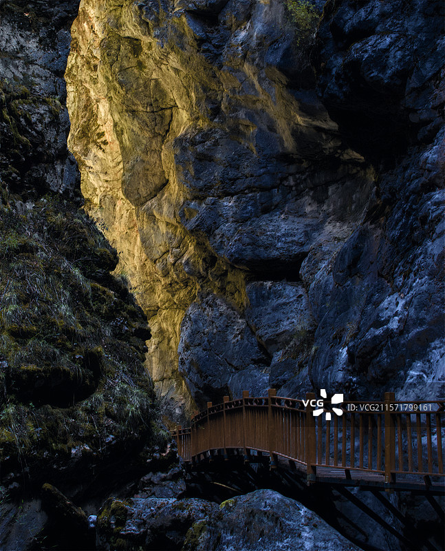甘肃甘南扎尕那润吾沟，木桥蜿蜒于嶙峋岩壁间，一束金光洒落，勾勒出峡谷神秘而壮丽的一隅。图片素材