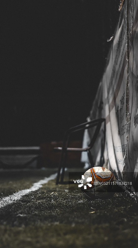足球特写, 暗调背景足球, 聚光足球, 舞台感足球视觉, 橙白足球近景, 人造草皮剪影, 暗幕背景图片素材