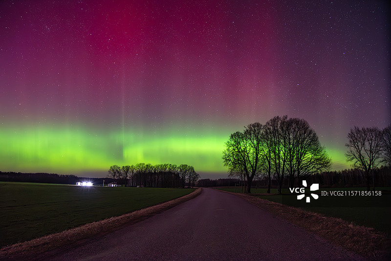 令人惊叹的粉色和绿色极光照亮了乡间道路上方的夜空，拉脱维亚的轮廓。图片素材