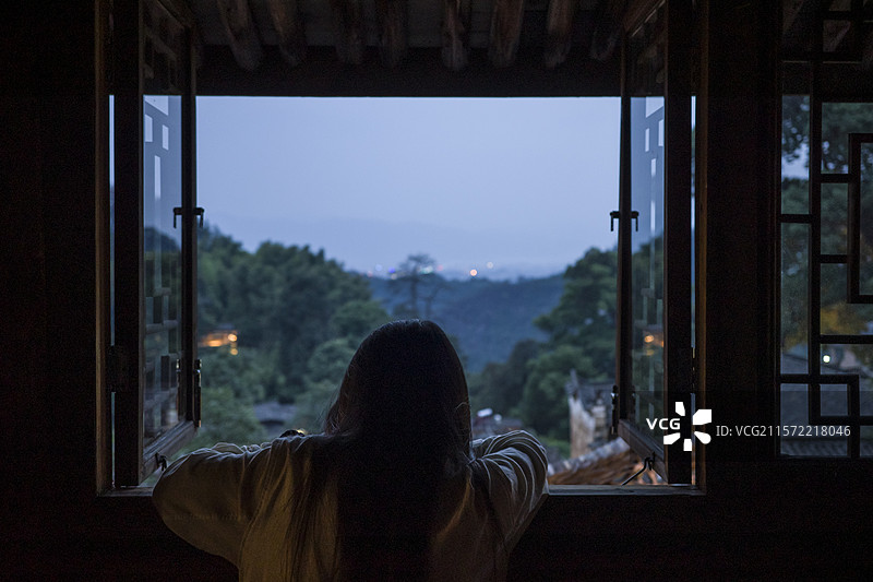 傍晚暮色下一个女人趴在中式民居窗户上看向窗外风景，浙江丽水松阳杨家堂村古村图片素材