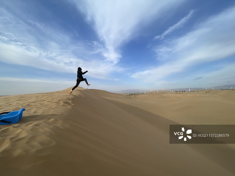 蓝天下沙丘上飞跃的男人图片素材
