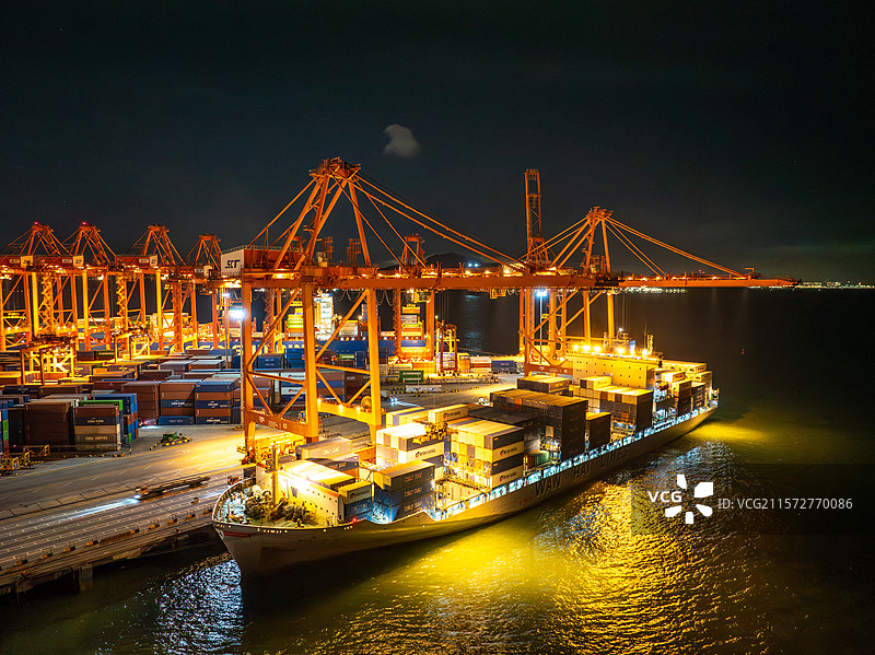 航拍夜晚灯火通明的深圳蛇口港码头，通过码头起重机在装卸远洋货轮上的集装箱夜景图片素材