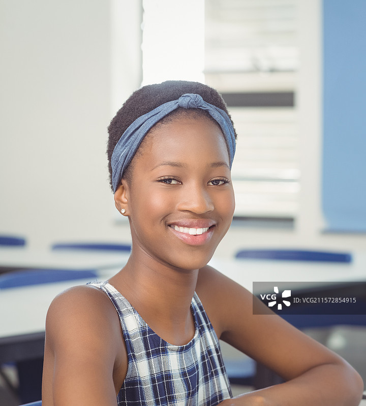 非裔美国女孩坐在学校的桌子旁，穿着格子上衣和头带，窗帘在旁。图片素材