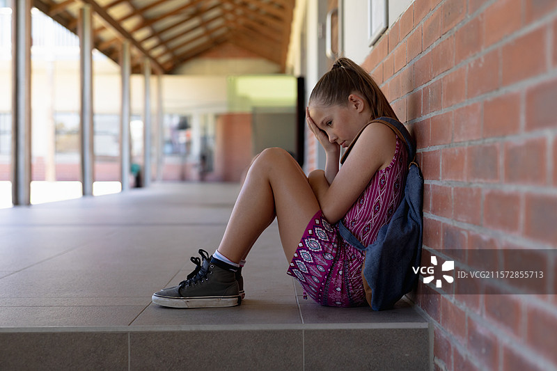 坐在学校走廊瓷砖台阶上的学生，背包靠在砖墙上，留有空白空间图片素材