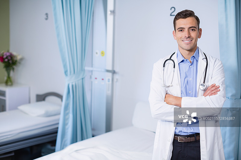 男医生站在医院病房床边的监测面板旁，手持听诊器，留有空白空间图片素材