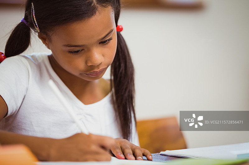 女孩学生在教室的木桌上拿着铅笔，正在打开的笔记本上写字。图片素材
