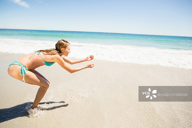 波浪轻轻拍打着湿沙，清澈的蓝天下，阳光在碧绿色的海水上闪烁。图片素材