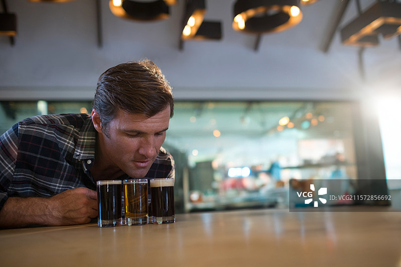 男子在酿酒厂的酒吧台前俯身检查啤酒品鉴飞行，暖色灯光下显得温馨。图片素材