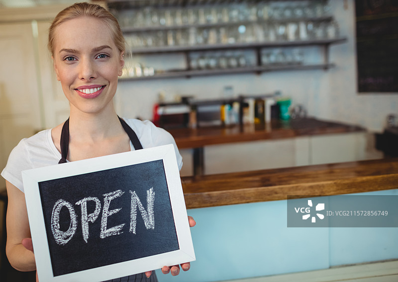 女人在咖啡馆柜台后面拿着“开放”黑板标志，旁边有咖啡机，留有空白空间图片素材