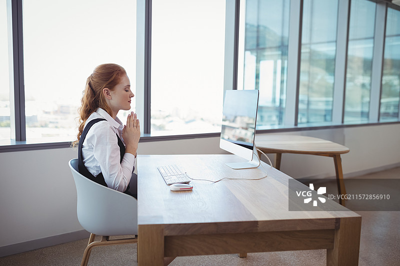 在办公室里，穿着背心的女性在桌子上冥想，使用显示器、键盘和鼠标，留有空白空间。图片素材