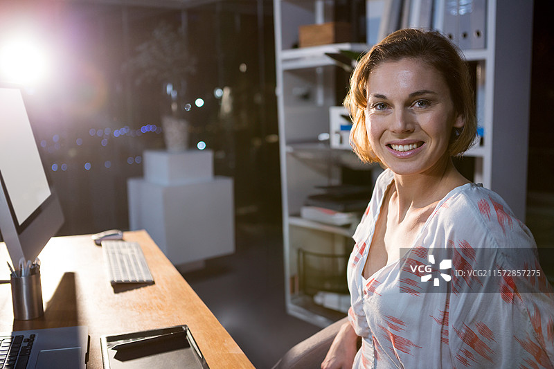 女人微笑着，在办公室的桌子上用手写板和手写笔工作，灯光下的夜晚。图片素材