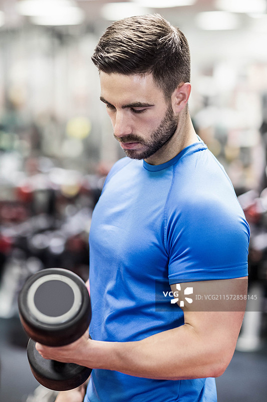 男性举重运动员在健身房穿着蓝黑色运动服进行哑铃弯举图片素材