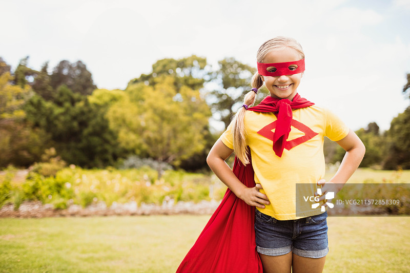 穿着红色眼罩和斗篷的学龄女孩在阳光明媚的公园里站着，留有空白空间图片素材