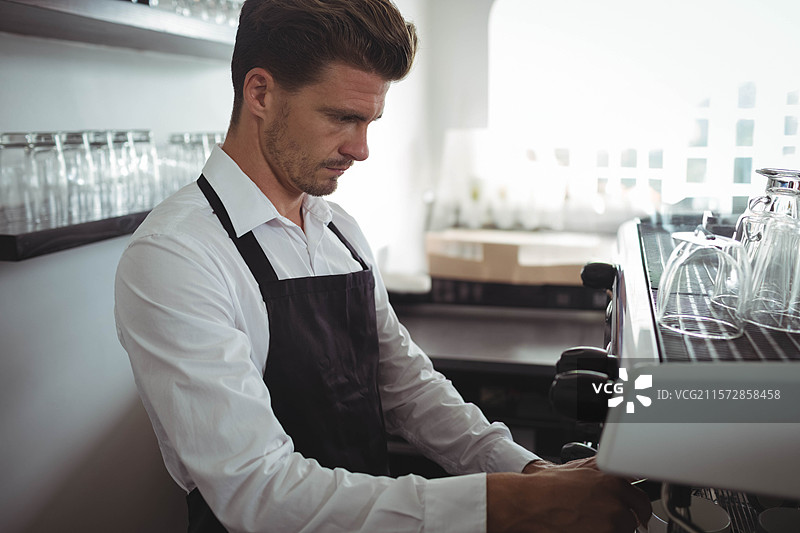 中年男子在咖啡柜台工作，操作着意式咖啡机，旁边有玻璃杯，留有空白空间图片素材
