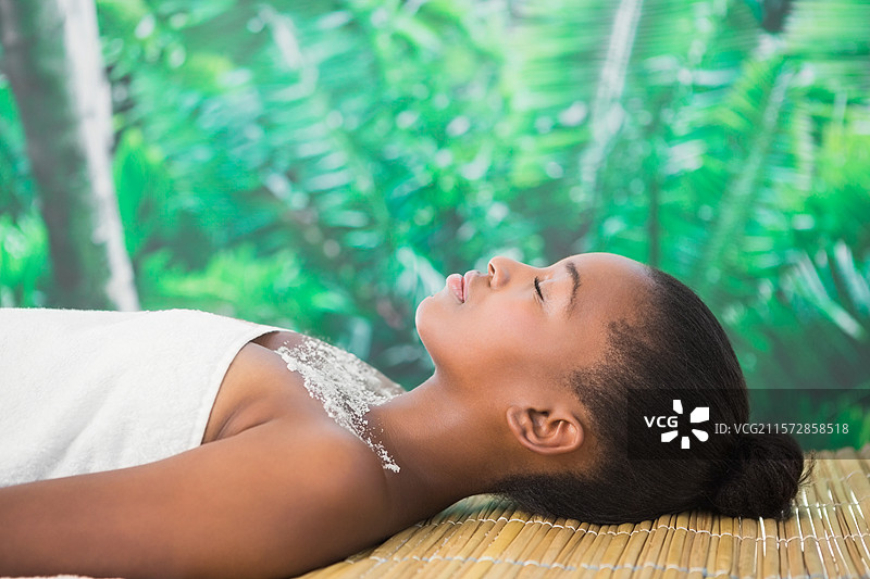 女子仰卧在竹垫上，裹着白色毛巾，展示热带水疗中的磨砂晶体图片素材