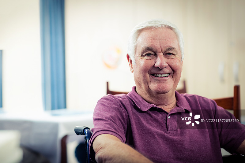 坐在餐厅里，微笑的老年人坐在轮椅上，桌上铺着白色桌布，窗帘是蓝色的。图片素材