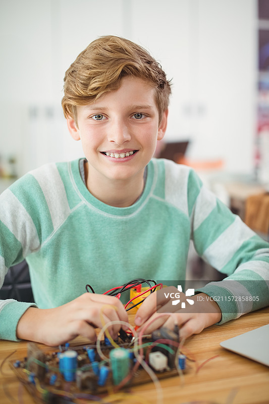 青少年男孩在工作台上使用面包板、导线和笔记本电脑组装电子电路图片素材